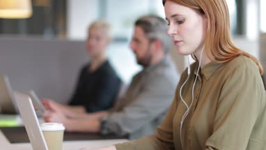 Businesswoman working on laptop with headphones in an open plan office