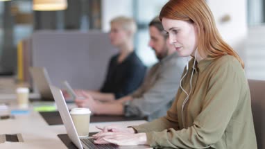 Businesswoman working on laptop with headphones in an open plan office