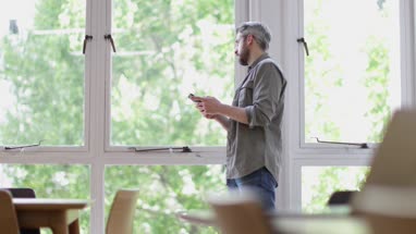 Businessman in office looking out of the window and at smartphone