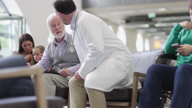 Senior Male talking to Doctor in a crowded hospital waiting room 
