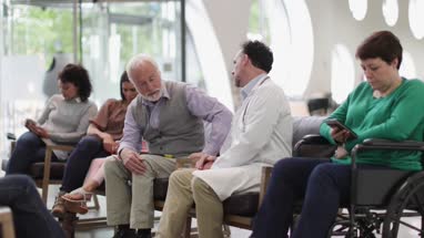Senior Male talking to Doctor in a crowded hospital waiting room 