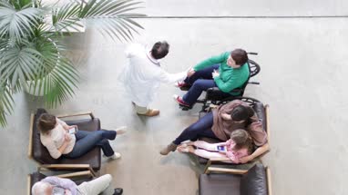 Overhead shot of Medical Doctor greeting woman in wheelchair in waiting room