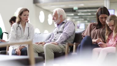 Senior Male talking to Doctor in a crowded hospital waiting room 