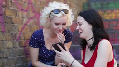 Female friends looking at smartphone and laughing in urban city