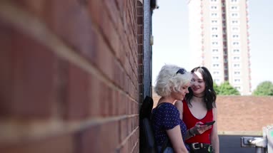 Female friends looking at smartphone and leaning against brick wall