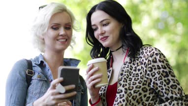 Female friends looking at smartphone and laughing outdoors in summer