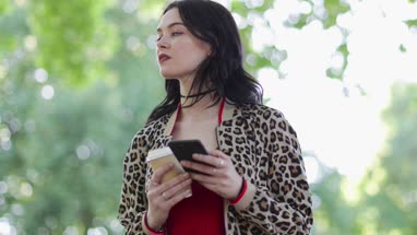 Trendy young adult female using smartphone in park in summertime