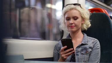 Young adult female travelling on train looking at smartphone
