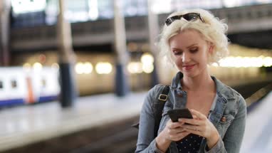 Young adult female on station platform using smartphone