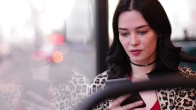 Young adult female travelling on bus looking at smartphone