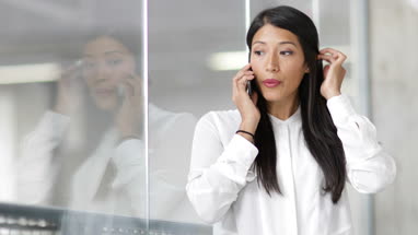 Businesswoman looking at reflection and using smartphone in an office