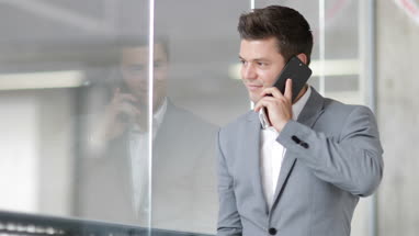 Businessman looking at reflection and using smartphone in an office
