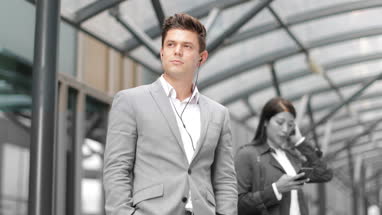 Businessman listening to podcast waiting for train at station