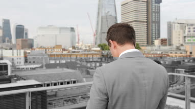 Businessman using smartphone looking out at London city skyline