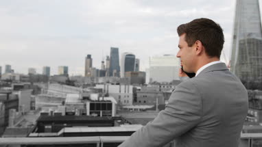 Businessman using smartphone looking out at London city skyline