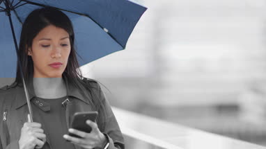 Businesswoman in city holding umbrella looking at smartphone