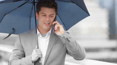 Businessman in city holding umbrella talking on smartphone