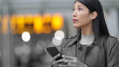 Commuter looking at train times at station holding smartphone