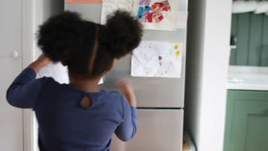 Girl proudly putting school work on refrigerator