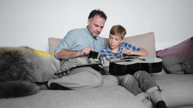 Father teaching son how to play guitar using a smartphone