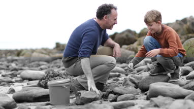 Father and Son looking at shells in rockpool on beach