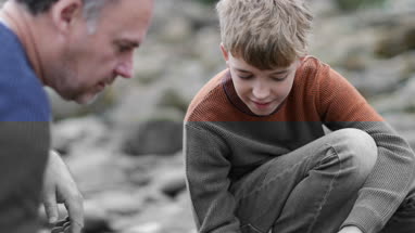 Father and Son looking at shells in rockpool on beach