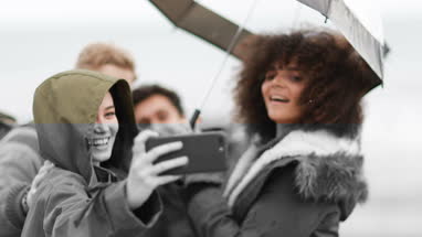 Group of young adult friends taking a selfie on a beach in the rain