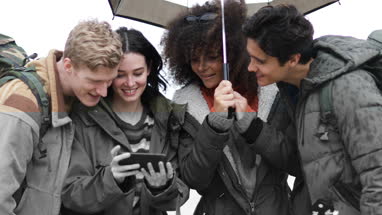 Group of friends using smartphone outdoors in rain