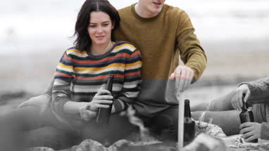 Group of young adult sitting around campfire with beer