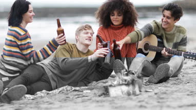 Group of young adult sitting around campfire with beer