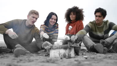 Group of young adult sitting around campfire toasting marshmallows