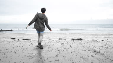 Young male skimming stones on a beach in winter
