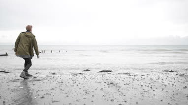 Young male skimming stones on a beach in winter