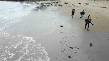 Aerial shot of friends running along beach holding hands