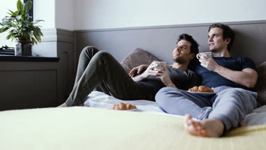 Young male couple relaxing with breakfast in bed