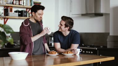 Young male couple having breakfast in kitchen