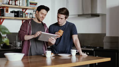 Young male couple looking at digital tablet in kitchen