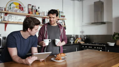 Young male couple looking at digital tablet in kitchen
