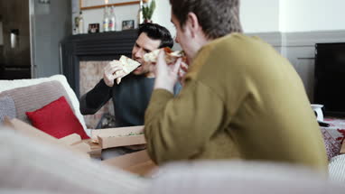 Young male couple eating pizza at home