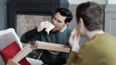 Young male couple eating pizza at home