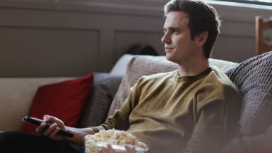 Young male streaming movie at home eating popcorn