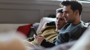 Young male couple relaxing on sofa streaming entertainment