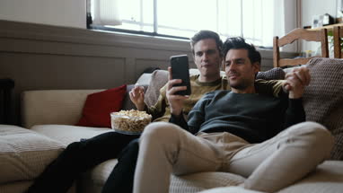 Young male couple relaxing on sofa streaming entertainment