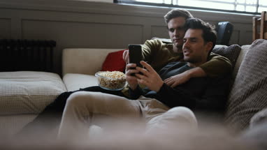 Young male couple relaxing on sofa streaming entertainment
