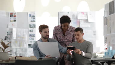 Designers looking at architectural plans and a smartphone in a creative workspace