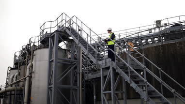 Industrial worker climbing staircase using a digital tablet on site