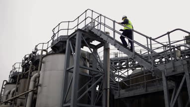 Industrial worker climbing staircase using a digital tablet on site