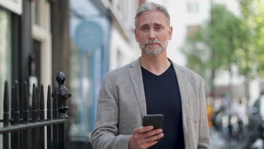 Portrait of mature male using smartphone outdoors in city