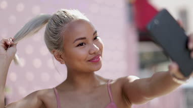Young adult female taking selfie with pink background