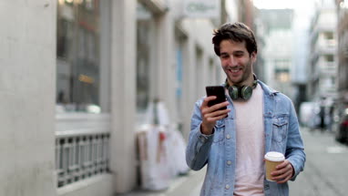 Young adult male walking down street looking at smartphone